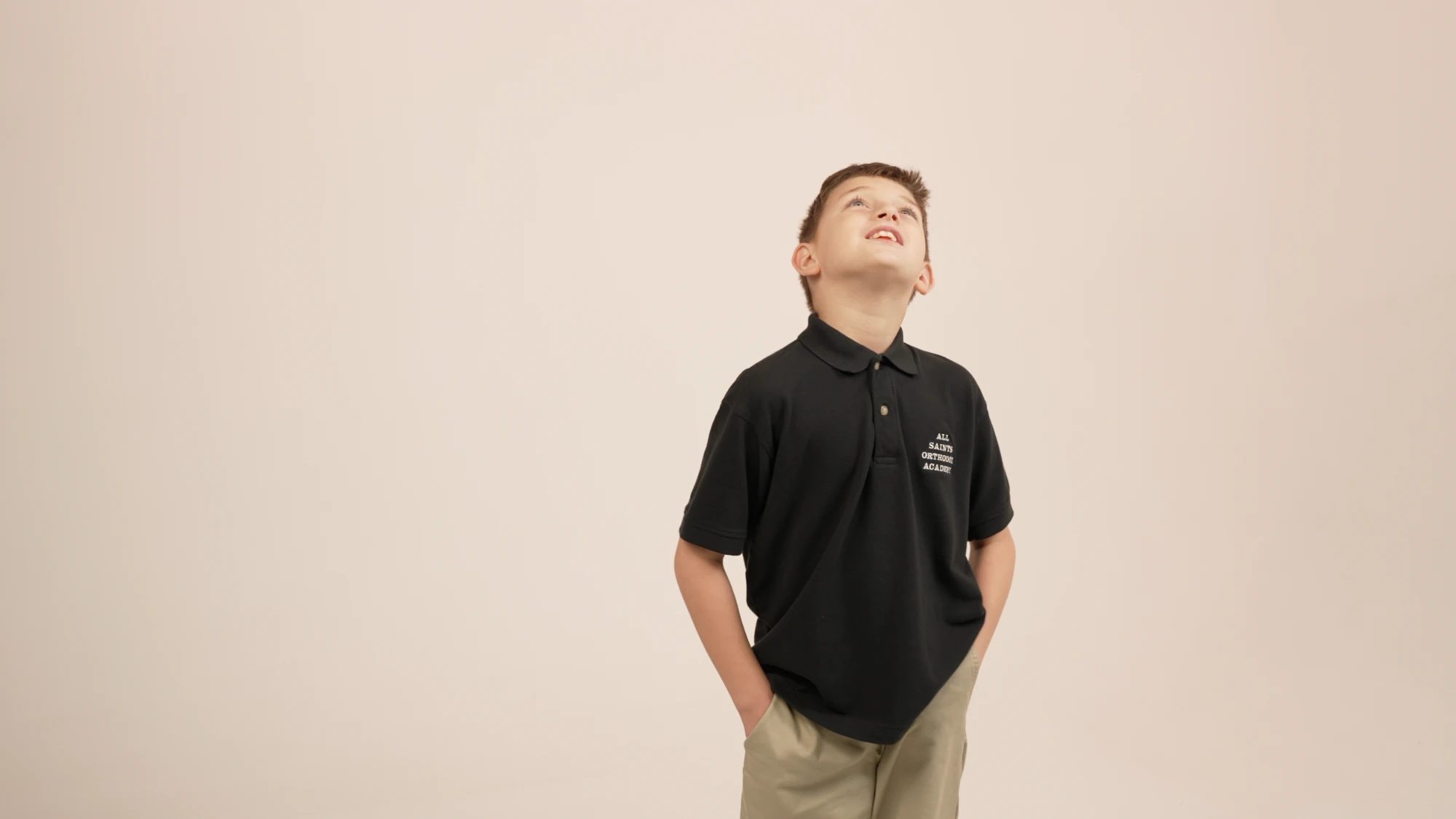 An All Saints student in a school polo, looking upward against a plain background