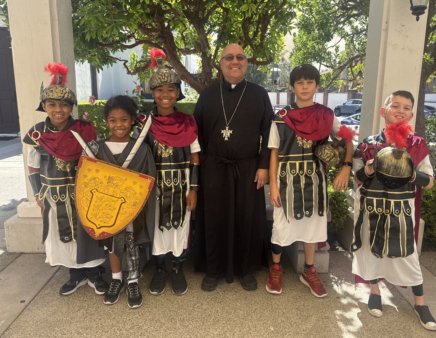 Five All Saints students in Roman centurion dress, standing with a priest outside the church