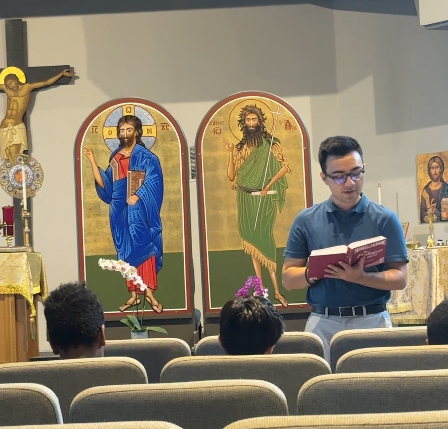 A reader standing before the icons of Christ and the Forerunner, reading aloud to the students