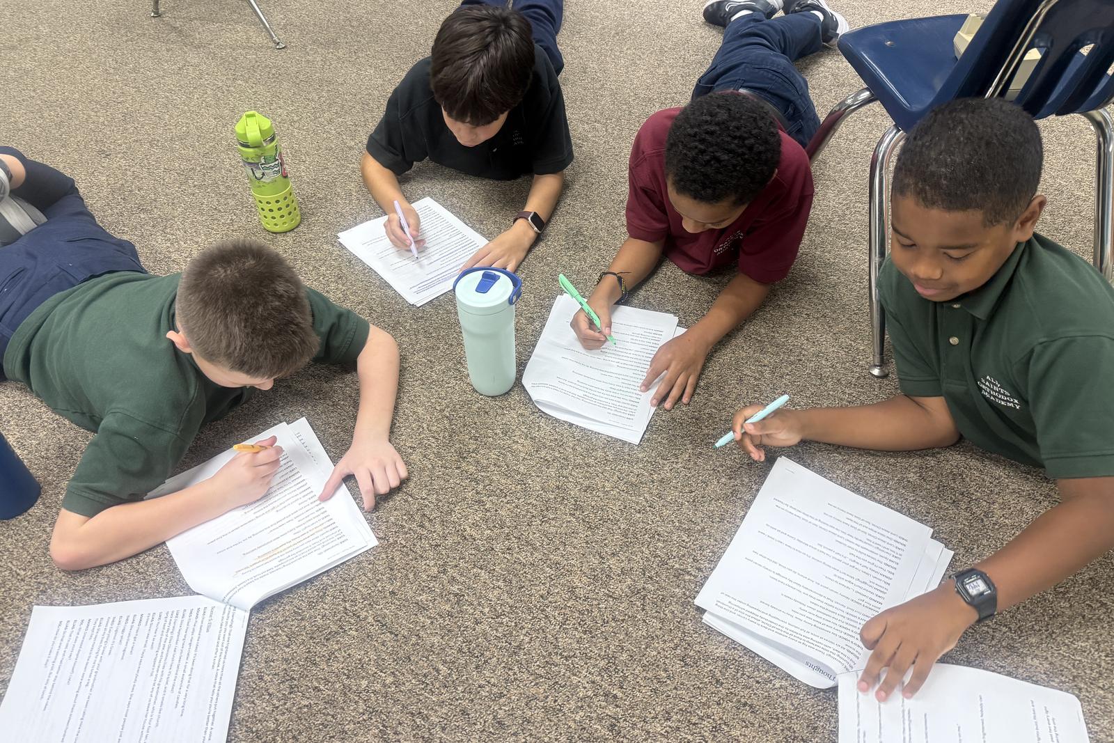 Four All Saints students lying on the floor annotating a text with highlighters