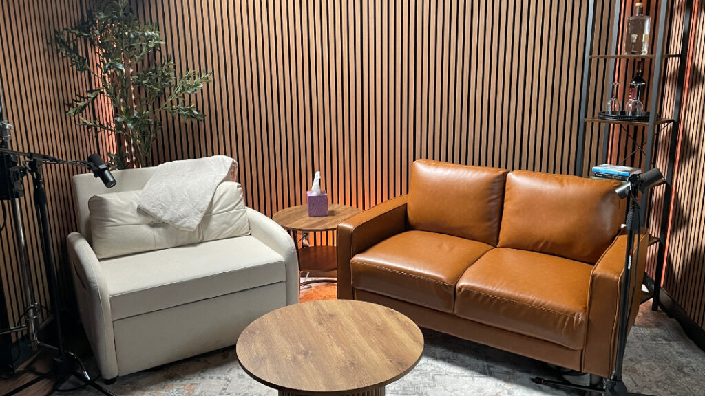 The interview set at Greek Fire Studios: two armchairs, a low wooden table, and two microphones on boom stands against a slatted wood wall