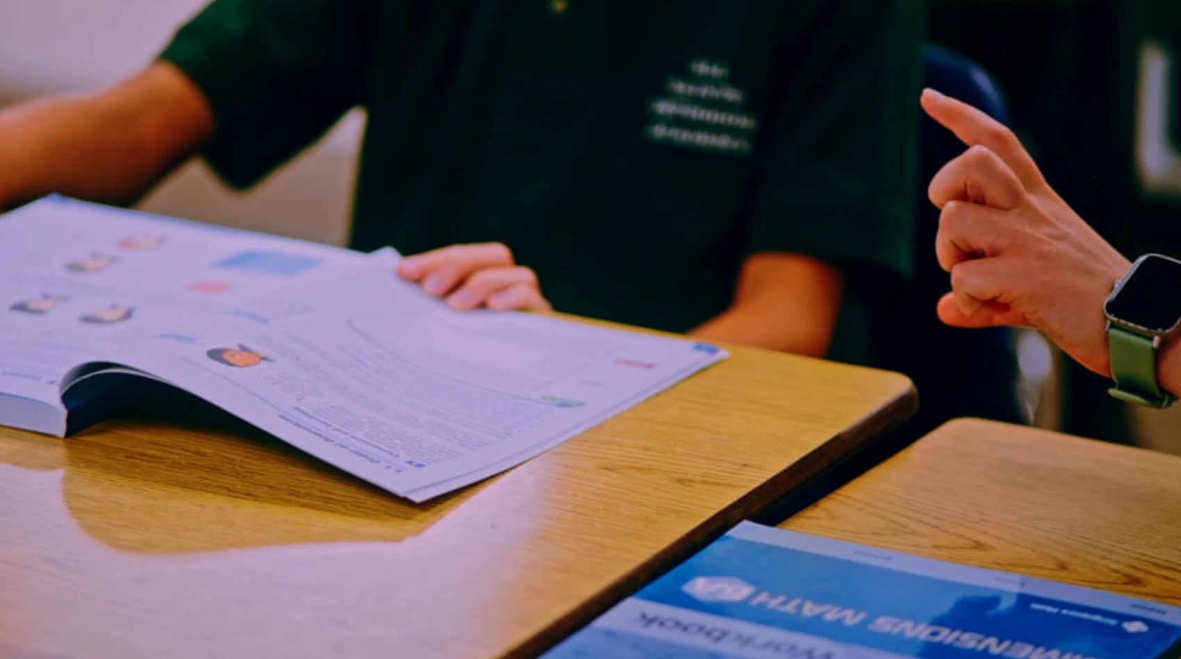 A teacher and a student working through a Dimensions Math workbook at a desk