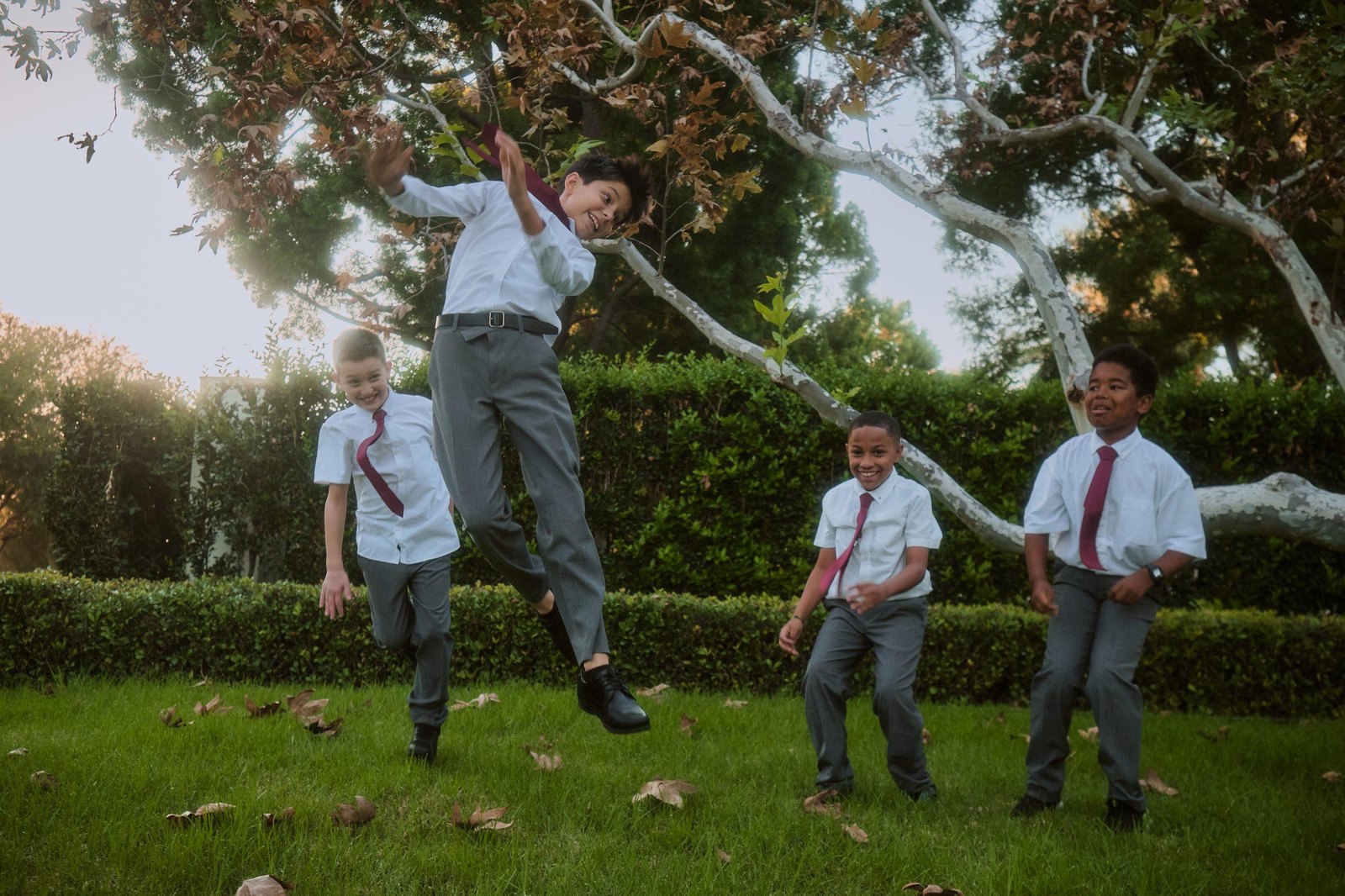 All Saints students in uniform playing on the lawn at golden hour, one mid-jump