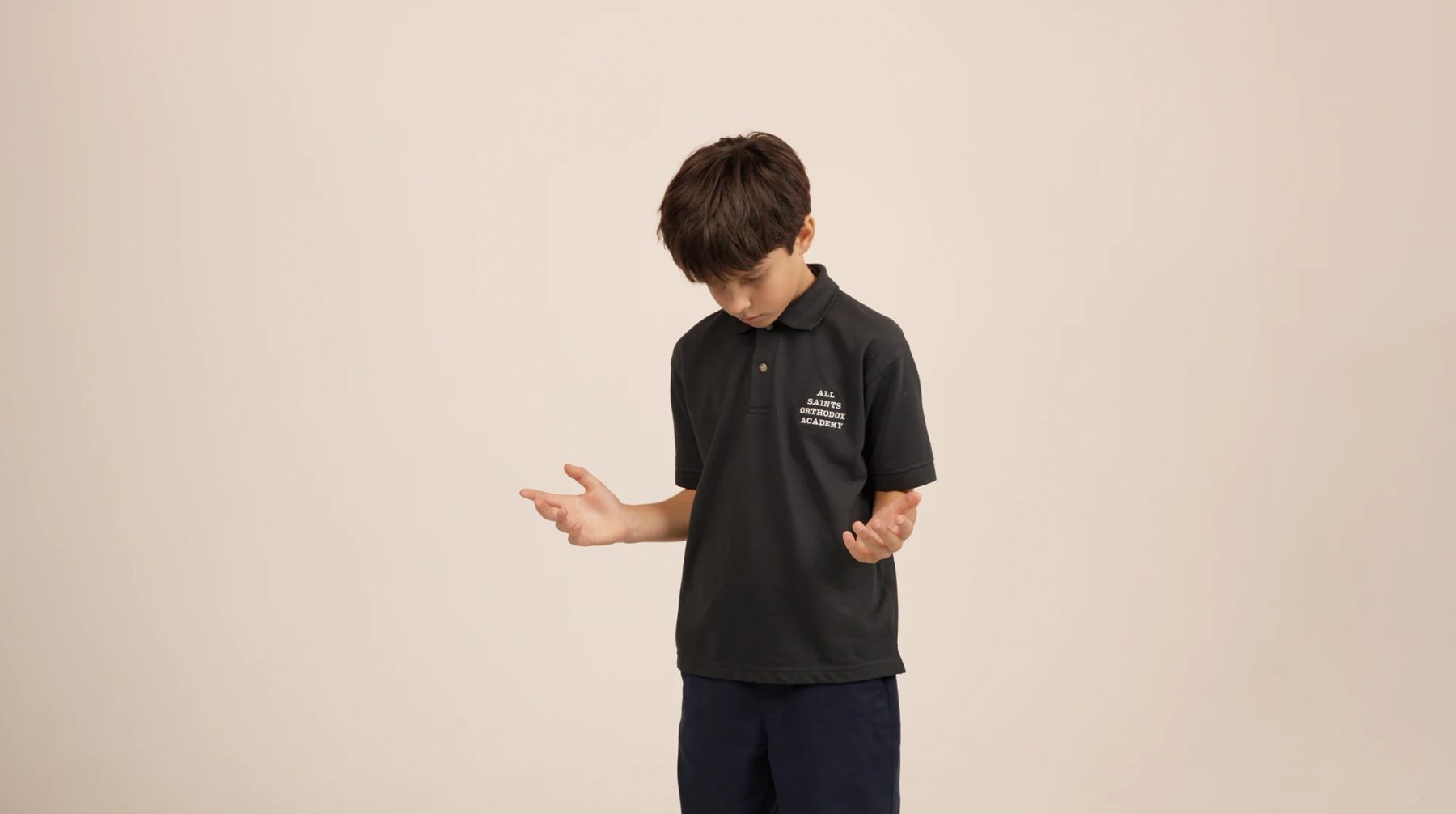 An All Saints student in a school polo, looking down with his hands open