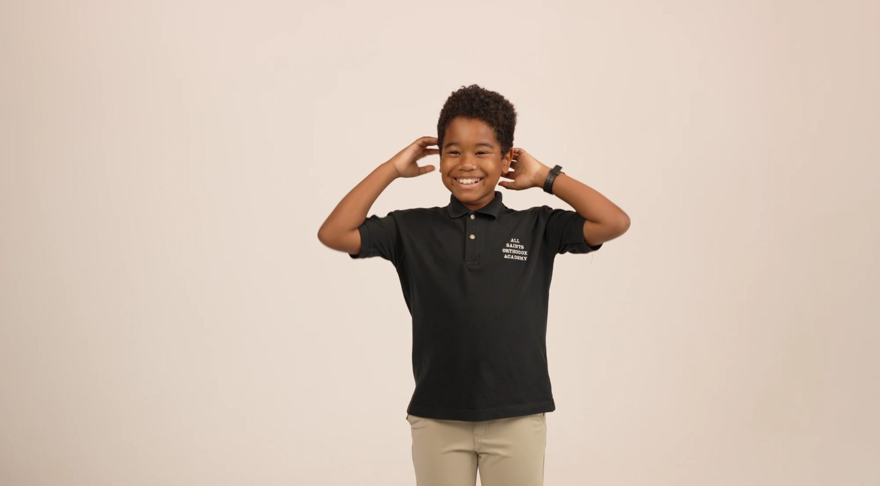 An All Saints student in a school polo, laughing with his hands behind his head