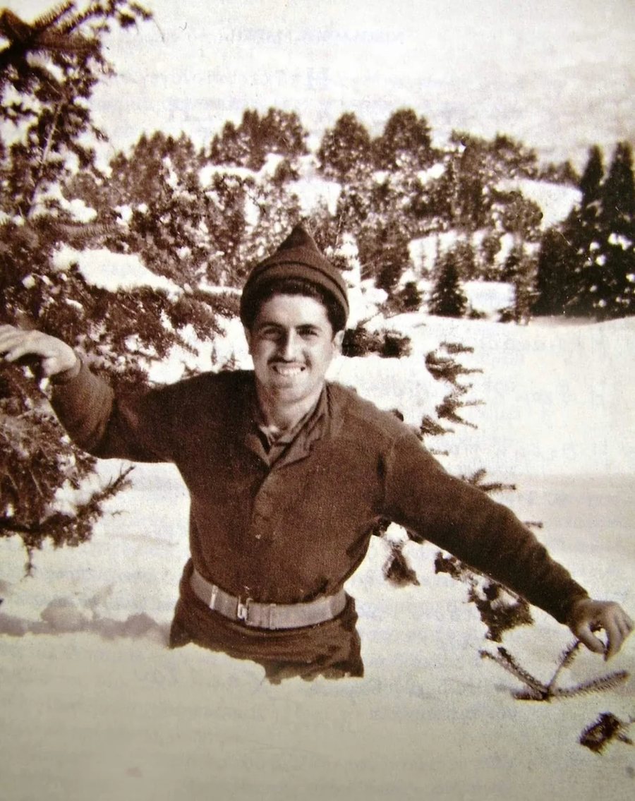 St. Paisios as a young soldier, smiling in deep snow in a knit cap and army sweater